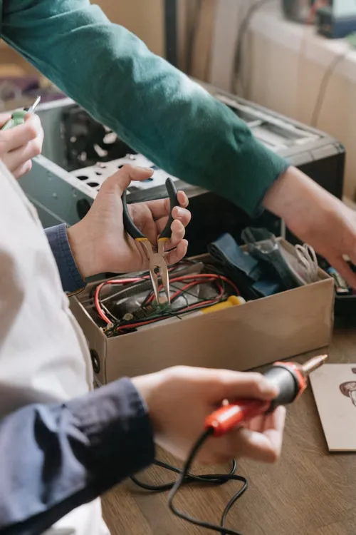Mani al lavoro con pinze e saldatore su un dispositivo elettronico aperto.